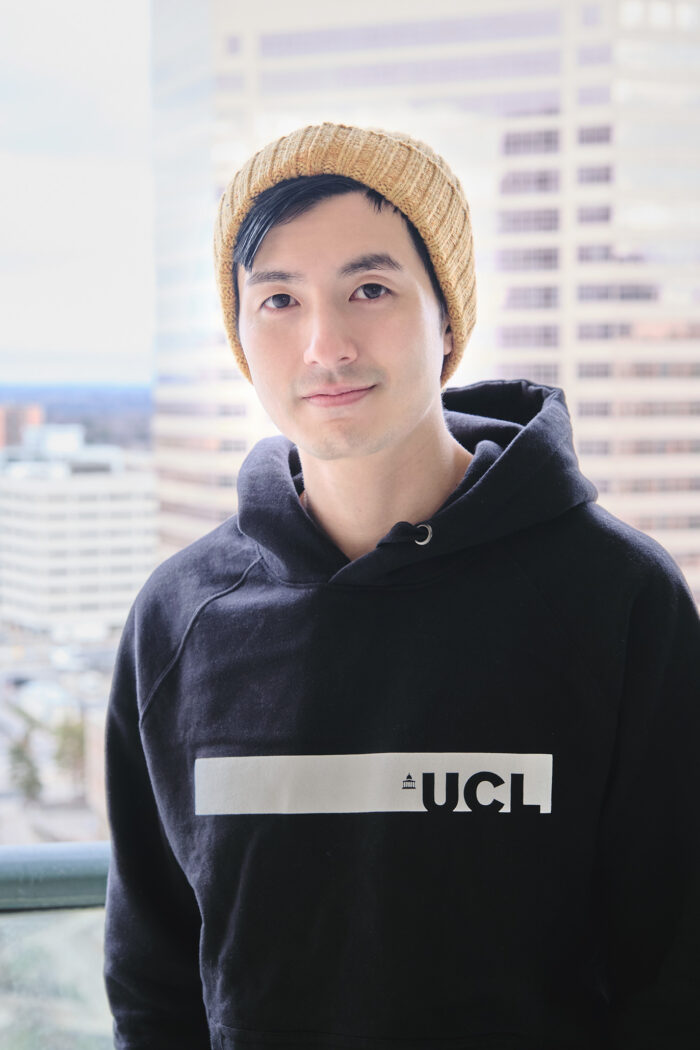 Photo of Savyn co-founder Vic Chiang, pictured wearing a black hoodie, yellow toque, and standing on a balcony overlooking a cityscape.
